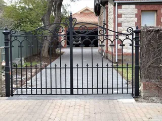 Black driveway gate with scrollwork between stone pillars