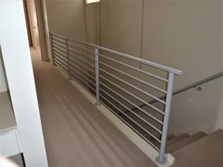Horizontal metal balustrade beside an indoor staircase