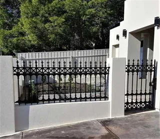Decorative black driveway gate and fence between white pillars