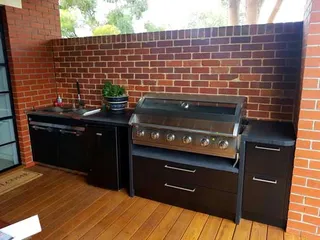 Black outdoor kitchen with barbecue and sink against a brick wall