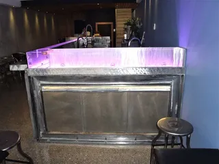 Front view of a metal bar counter with illuminated glass surround