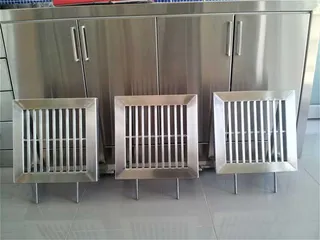 Three square stainless steel floor grates in front of cabinetry