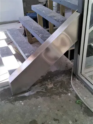 Angled stainless steel panel beside concrete stairs under construction