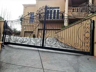 Large ornate wrought iron driveway gates on a sloping driveway
