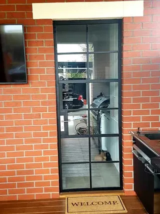 Black framed glass pedestrian door set into a brick wall