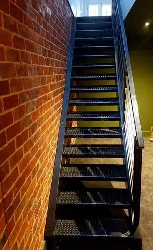 Black steel staircase with perforated metal treads beside a brick wall